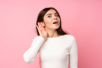 Young woman over isolated pink background listening something