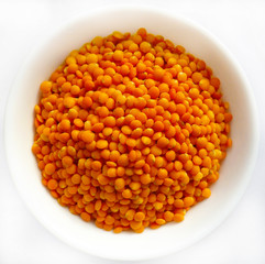 Red split lentil in white bowl isolated on white background, top view, closeup. Healthy food background.
