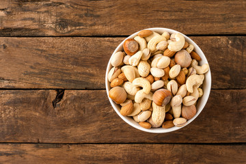 Nuts: almonds, pistachios, peanuts, hazelnuts and cashews in bowl on wooden background with copyspace