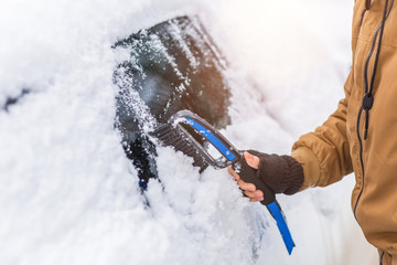 Vehicle and people concept - man cleaning snow from car with cleaning tool