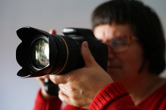 Adult woman dressed in red taking pictures with her camera on a grey background.