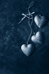 Love Valentines day greeting card with three silver hearts on rope cord over old dark metal background. Top view, copy space. Color of the year 2020 classic blue toned