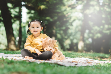 Little asian girl hugging her teddy bear in a park. Concept of happiness and childhood