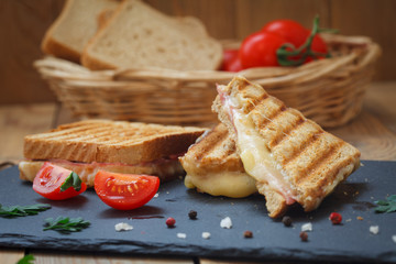 Club or toast sandwiches on black tray. Grilled sandwiches with ham salami, tomato and melted...