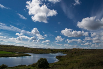  Blue sky with white cumulus clouds. Quiet river in a green valley.