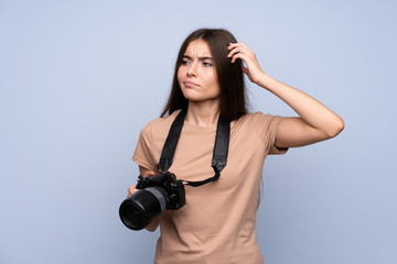 Fototapeta premium Young woman over isolated blue background with a professional camera and thinking