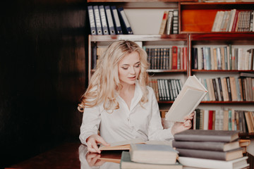 the girl sitting in the library reading books is preparing for the exam