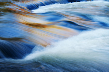 Bond Falls cascade captured with motion blur and illuminated by reflected color from sunlit autumn...