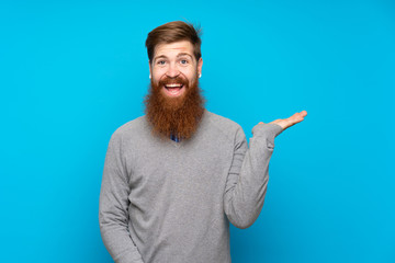 Redhead man with long beard over isolated blue background holding copyspace imaginary on the palm...