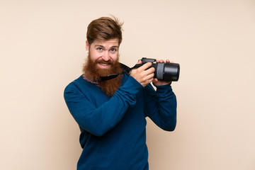 Redhead man with long beard over isolated background with a professional camera
