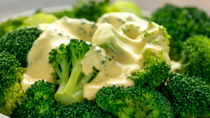 Broccoli with cheese sauce in white bowl on wooden table