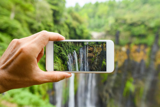 A tourist is taking pictures with a smartphone to the beautiful Tumpak Sewu Waterfalls. Tumpak Sewu Waterfalls are a tourist attraction in East Java, Indonesia.
