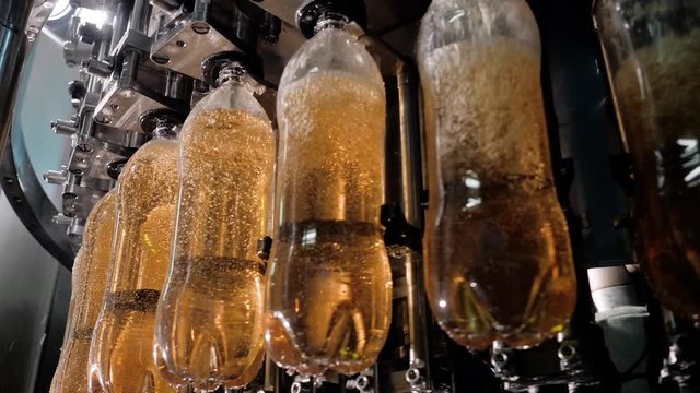 Plastic bottles pass across conveyor and automatically are filled carbonatded drinks, liquids. Beverage bottling and packaging production line on modern equipment, close-up. Bottling plant concept.