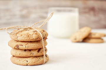 Chocolate chip cookies with a glass of milk on a light gray background and a wooden wall. Copy space. Banner.