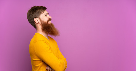 Redhead man with long beard over isolated purple background in lateral position