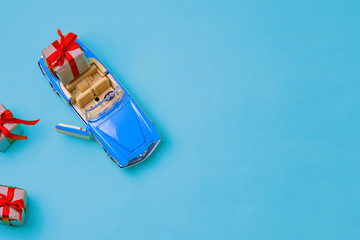 Miniature mini toy.Blue toy car with open top convertible carrying a gift with a red bow on a blue background. View from above. Miniature mini toy.