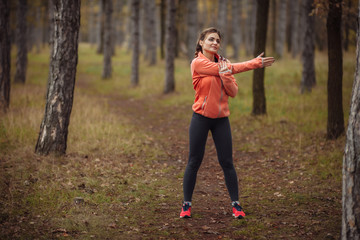 Young attractive sport woman in sportswear doing stretching exercise for hand in autumn forest....