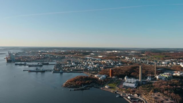 Slow descending aerial drone view of industrial area in Gothenburg, Sweden, with Rya Forest Nature Reserve visible lower right behind chimney