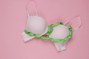 Srylish women underwear bra and tape measure on pink pastel background. Breast loss concept, measuring bust. Top view - obrazy, fototapety, plakaty