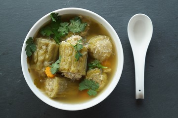 Close up bitter melon with minced pork and glass noodle clear soup top view. Thai food bitter melon with minced pork clear in white bowl near by spoon.
