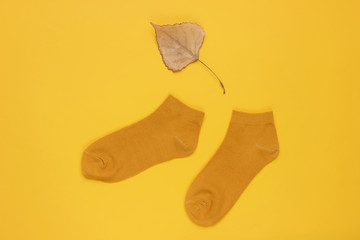 Autumn time. Orange socks with a dry fallen leaf on a yellow background. Top view