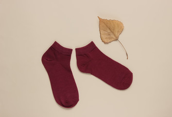 Autumn time. Red socks with dry fallen leaf on beige background. Top view