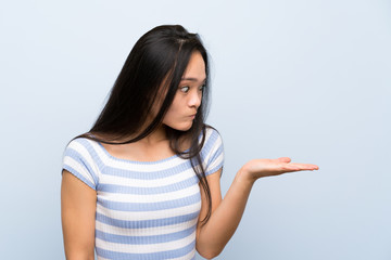 Teenager asian girl over isolated blue background holding copyspace imaginary on the palm