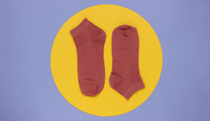 Red socks on a purple background with a yellow circle in the middle. Minimalistic fashion still life. Top view