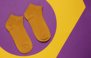 Orange socks on purple yellow background. Minimalistic fashion still life. Top view