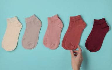 Female hand makes a choice of a pair of casual colored socks on a blue background. Top view