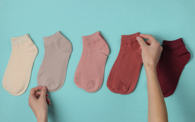Female hand folds a colored socks on blue background. Top view