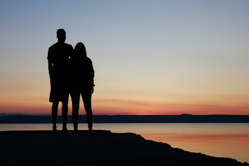 Young couple in love watching sunrise. Silhouette of standing couple. Standing by the sea. 