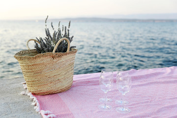 Nice picnic arrangement. Pink banket by the sea with vine glasses and picnic basket filled with lavender. 