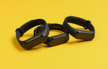 Three smart bracelets on yellow background. Modern gadgets for sports and everyday activities
