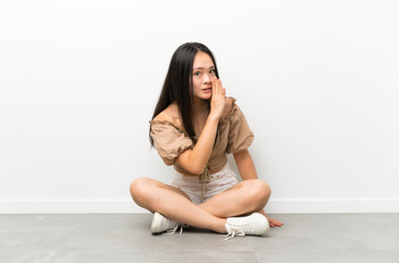 Teenager asian girl sitting on the floor whispering something