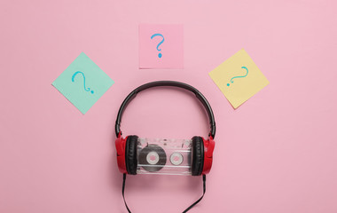 Wired headphones with audio cassette and question marks on memo pieces of paper on pink pastel...