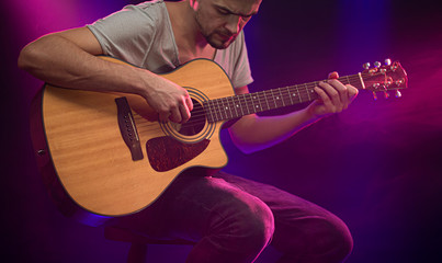 Fototapeta na wymiar The musician plays an acoustic guitar. Beautiful background with colored light rays.