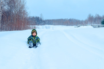 Cute Asian little child boy a green colorful jumpsuit  portrait  smiling on a  white fluffy snow in Siberia. Happy baby playing in the park outdoors in snow on cold winter day. With a smile of happy