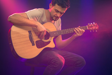 Fototapeta na wymiar The musician plays an acoustic guitar. Beautiful background with colored light rays.