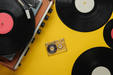 Old-fashioned vinyl player with records and audio cassette on yellow background. Retro media 70s....