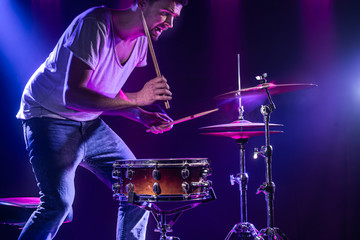 A drummer plays drums on a blue background. Beautiful special effects of light and smoke. The process of playing a musical instrument.