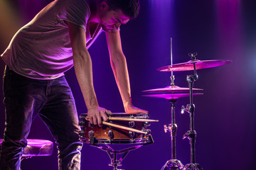 The drummer plays the drums. Beautiful blue and red background, with rays of light. Beautiful special effects smoke and lighting. The process of playing a musical instrument. Close-up photo.