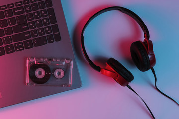 Lptop with headphones and audio cassette. Neon blue-red gradient light. Retro wave, pop culture, DJ...
