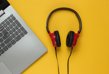 Laptop and dj headphones on yellow pastel. Top view
