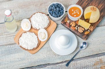Boiled egg in egg cup and sandwich with cheese with slice egg, raisin, honey, parmesan, nut and pumpkin seed. Healthy breakfast on a wooden table