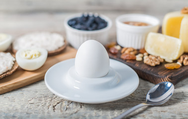 Boiled egg in egg cup and sandwich with cheese with slice egg, raisin, honey, parmesan, nut and pumpkin seed. Healthy breakfast on a wooden table