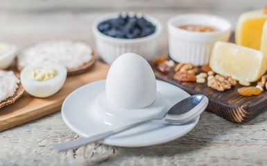 Boiled egg in egg cup and sandwich with cheese with slice egg, raisin, honey, parmesan, nut and pumpkin seed. Healthy breakfast on a wooden table