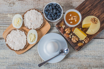 Boiled egg in egg cup and sandwich with cheese with slice egg, raisin, honey, parmesan, nut and pumpkin seed. Healthy breakfast on a wooden table