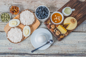 Boiled egg in egg cup and sandwich with cheese with slice egg, raisin, honey, parmesan, nut and pumpkin seed. Healthy breakfast on a wooden table