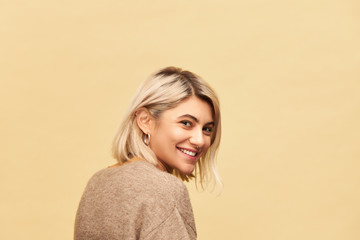 Back view of gorgeous positive young European female wearing warm cozy jumper turning head round...